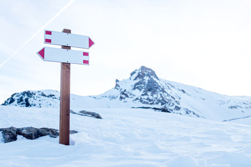 Two white signs indicating a path intersection in the mountains during winter