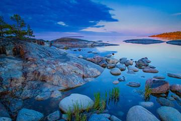 Karelia. Rocky Islands in lake Ladoga. Skerries of lake Ladoga. Northern nature. The island in the distance is illuminated by the setting sun. Evening in Karelia. Travel to Russia. - obrazy, fototapety, plakaty
