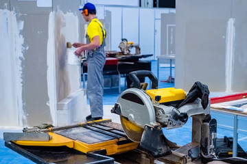 Circular saw for cutting stone and tiles. A man makes repairs in the shop for the processing of stone. Plaster walls in the room. Equipment for cutting stone slabs.