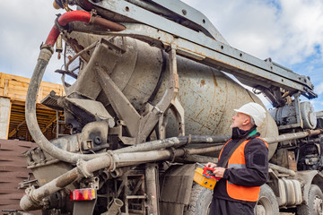 A man in a white helmet holding a remote control supply of cement.Worker directs the unloading of cement. Cement is fed from the mixer. Remote control concrete mixer. Man controls the flow of concrete