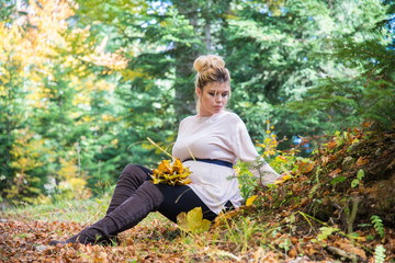 Young pregnant woman in nature enjoying autumn sun outdoors.