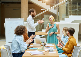 Obraz premium Charming young female designer with short blonde hair, dressed in long green dress, keeps hand on heart with broad teeth smile, expresses pleasant feelings