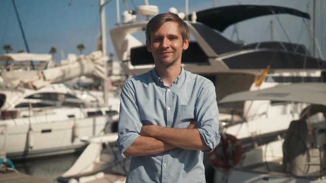 Man dressed in casual wear near yacht. Happy adult bearded yachtsman close-up portrait. Handsome sailor smiling during regata on a sea or river.
