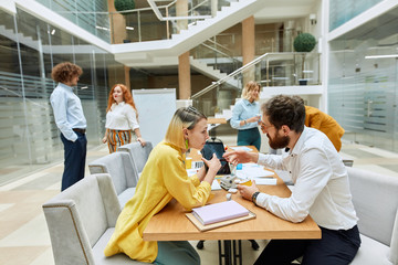 Concentrated mindful wears casual outfit, holds laptop, indicates with finger at screen, shows creative design project to interested bearded man in spectacles