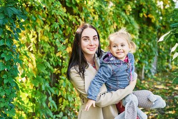 Fototapeta premium Happy family on autumn walk. Mother and daughter walking in Park and enjoying beautiful autumn nature. Hello, Autumn! Happy loving family having fun. Autumn leaf fall