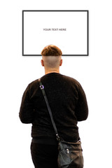 A man with an unusual haircut stands on a white wall and looks at a empty bilboard. Rear view - image