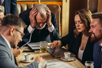 Ambitious people vividly talking at nice table while wise elderly leader bowing head over the papers carefully studying information. Closeup. Business team