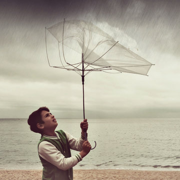 Boy standing on beach holding a broken umbrella in the rain, Spain