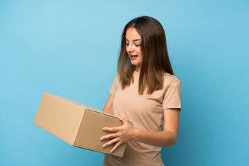 Young brunette girl over isolated blue background holding a box to move it to another site