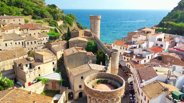 Aerial, drone shot, over towers and buildings, towards the Playa es Codolar and Mirador platja des Codolar, on a sunny, summer day, in Tossa de Mar, Girona, Catalonia, Spain
