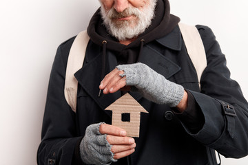 unrecognizable old man wearing street clothes holding house made of cardboard, dream about shelter....