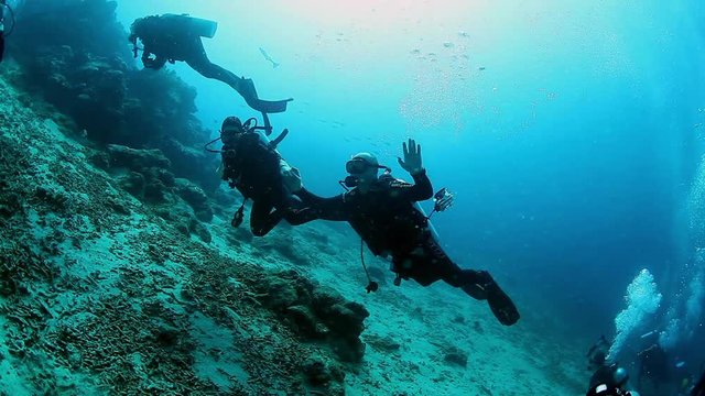 Man and woman divers waving hand hello camera in underwater ocean of Fiji. Concept of diving as lifestyle, sports and outdoor activities.