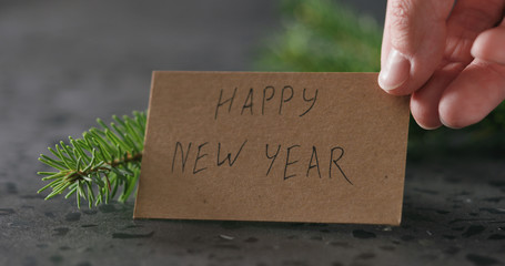 man hand put happy new year card next to spruce twig