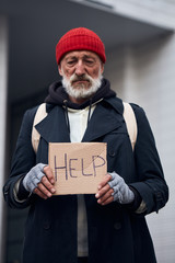 Old grey bearded man standing with sign HELP, asking for money, food, shelter. Concept of homeless person, poverty, despair