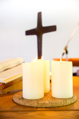 three white lightened candles in a church behind with a crucifix an a book