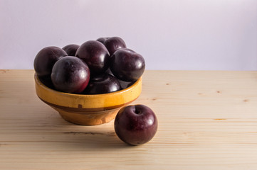 still life with bowl with plums, isolated on wooden background