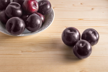 Still life with a plate with plums and three loose on wooden background