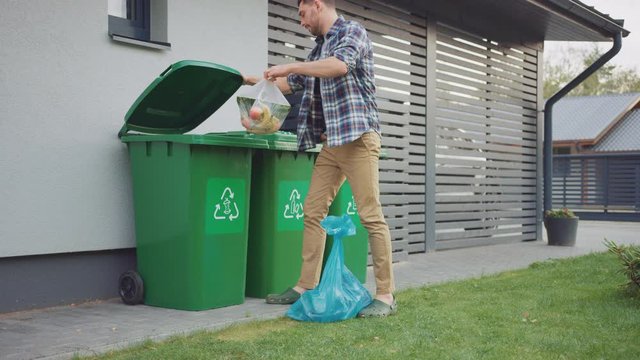 Caucasian Man is Walking Outside His House in Order to Take Out Two Plastic Bags of Trash