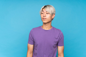 Young asian man over isolated blue background making doubts gesture looking side