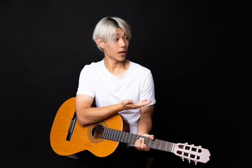 Young asian man with guitar over black background with surprise facial expression