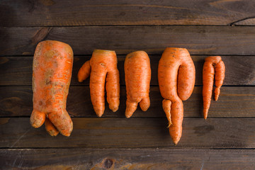ugly carrots lined up on brown wooden table top view flat lay