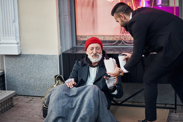 Responsive businessman in black suit proposing box filled with warm food and coffee to thankful...