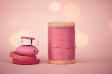 Stack of buttons with roll of thread over lights at background closeup. Selective focus.