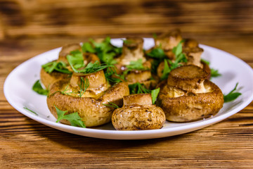 Plate with baked champignons, dill and parsley on a wooden table