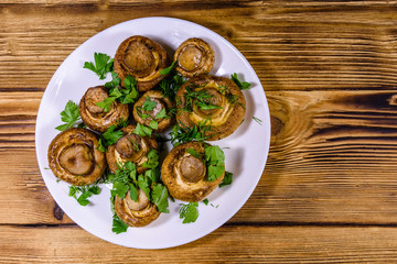 Plate with baked champignons, dill and parsley on a wooden table. Top view