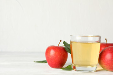 Apples and glass with juice on wooden background, space for text