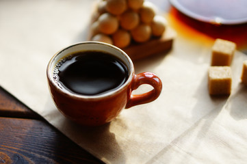 Hand made orange ceramic cup of black coffee on kraft paper. Wooden pyramid puzzle and cane sugar cubes in the blurred background