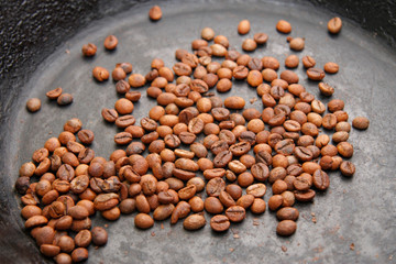 Green coffee beans roasting on the black pan