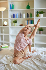 Obraz na płótnie Canvas Charming and smilng fitness woman in pajamas doing exercises at home on bed. Healthy lifestyle concept