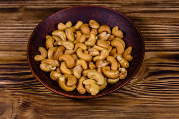 Ceramic plate with roasted cashew nuts on a wooden table