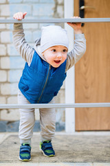 A brightly dressed two-year-old baby is playing on the stairs. He smiles cheerfully.