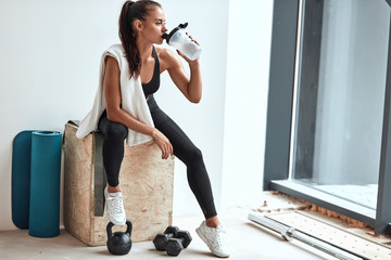 Fototapeta Young woman in leggins with towel on shoulders drinking water after fitness training obraz