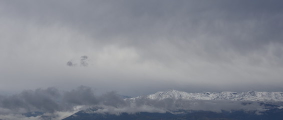 Morning view of Sierra Nevada between clouds covered by the first snowfall of autumn