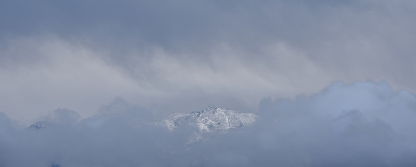 Morning view of Sierra Nevada between clouds covered by the first snowfall of autumn
