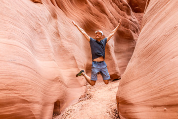 Man happy hiker jumping up arms raised by red wave shape formations at Antelope slot canyon in Arizona on footpath trail from Lake Powell © Kristina Blokhin
