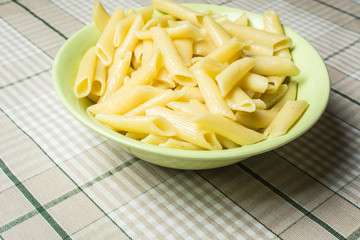 Tubular pasta in green plate on kitchen table.