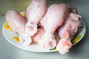 Raw chicken legs on a large plate drain from the water after washing.