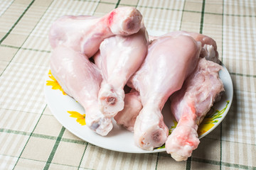 Raw chicken legs on a large plate drain from the water after washing.