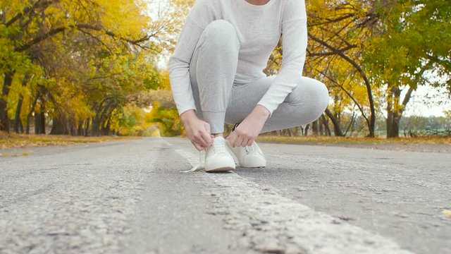 runner tying shoelaces on asphalt track in autumn nature, young woman get ready to start running, girl engaged in sport outdoors, concept healthy lifestyle and body care