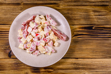 Salad with crab sticks, cheese and tomatoes dressed with mayonnaise on a wooden table. Top view