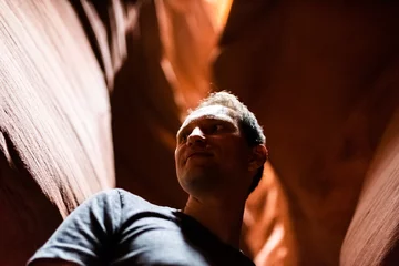 Acrylglasbilder Braun Low angle view of young happy man inside Upper Antelope slot canyon in Arizona looking at dark rock sandstone wave shape formations  © Kristina Blokhin