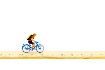 Miniature people ride bicycles on wooden ruler.