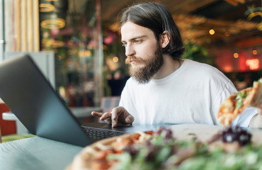 Hot delicious pizza is waiting for a youngster working keen by a laptop