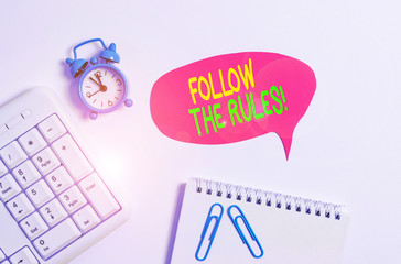 Word writing text Follow The Rules. Business photo showcasing go with regulations governing conduct or procedure Blank paper with copy space on the table with clock and pc keyboard