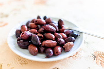 Closeup macro of purple red marinated kalamata olives on white plate in Italy or Greece for serving as appetizer on table party setting