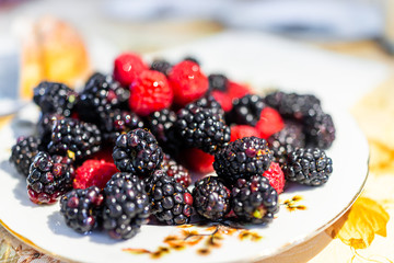 Closeup plate of raspberries and blackberries berries on table in as party setting serving harvested healthy fruit showing texture